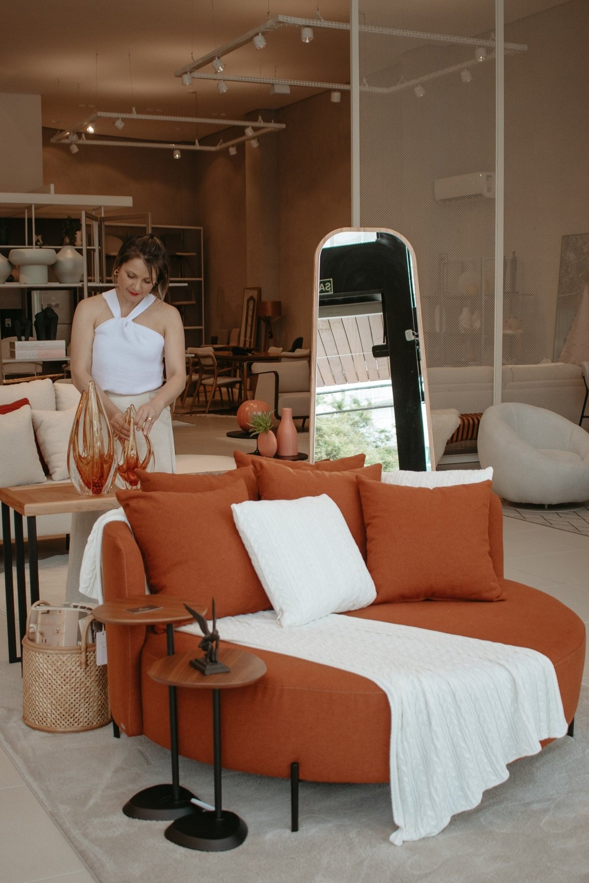 Poltrona redonda com almofadas soltas e manta em loja de móveis com mesas laterais e espelho