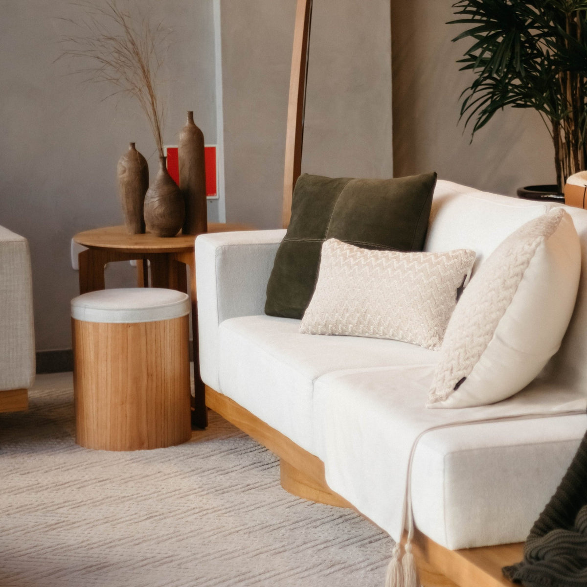Puff com base de madeira ao lado de sofá em sala de estar com mesa lateral e vasos