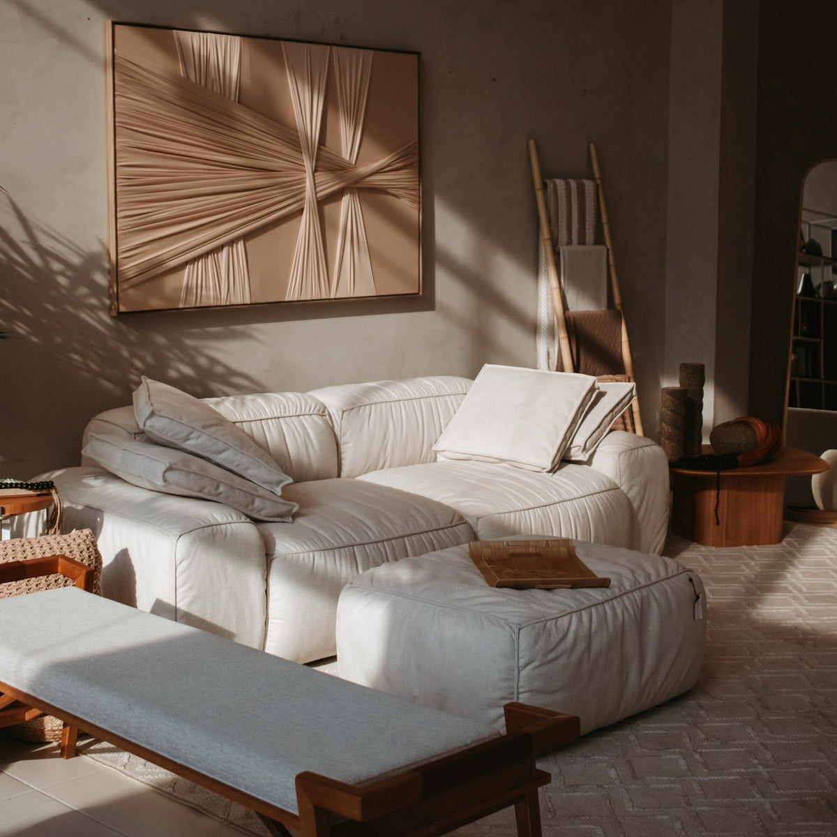 Sofá com puff em sala de estar com quadro em relevo, escada decorativa e banco de madeira