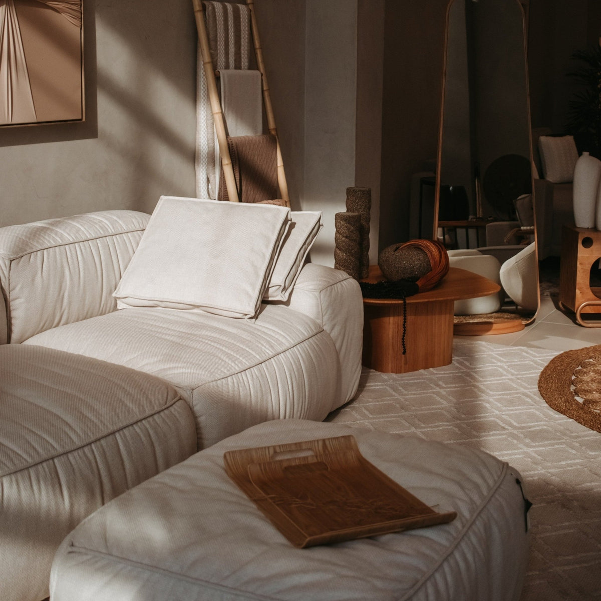 Sofá com puff e bandeja de madeira em sala de estar com mesa lateral de madeira e luz natural